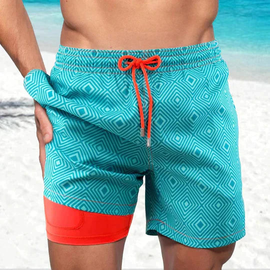 Noah teal geometric print swim shorts, front view on beach